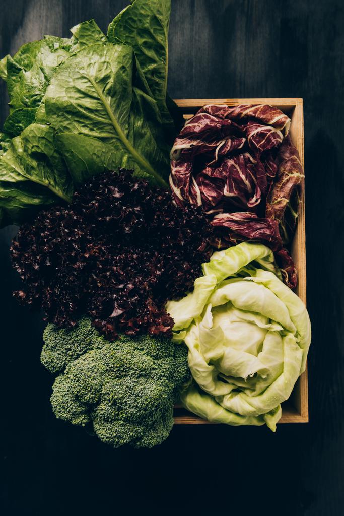 top view of different cabbages and salads in wooden box on grey dark table - Photo, Image