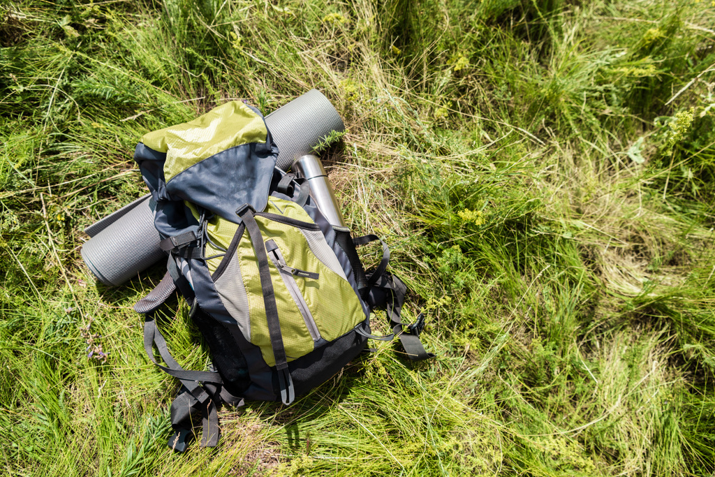 high angle view of backpack with tourist mat and thermos on green grass outdoors - Photo, Image