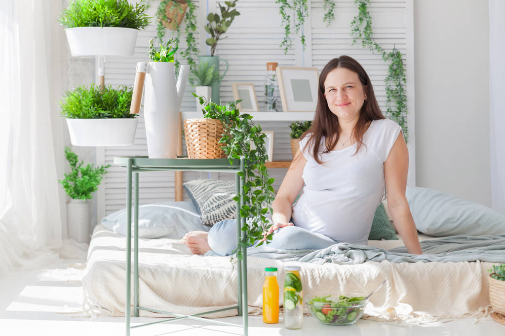 Молода вагітна жінка позує в світлому сучасному скандинавському інтер'єрі спальні
 - Фото, зображення