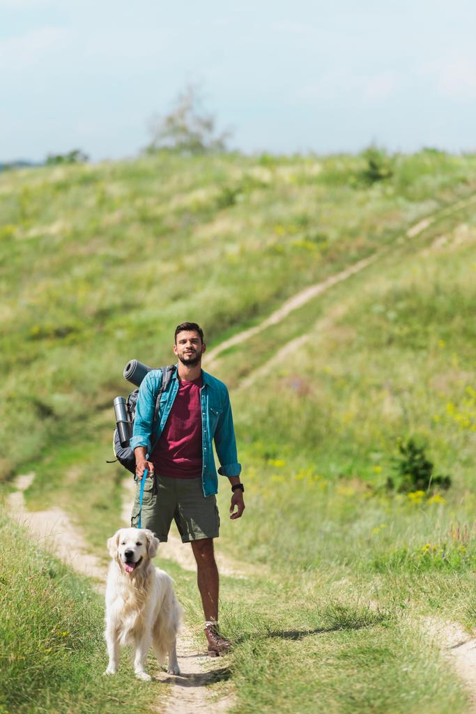 viajero masculino caminando con perro en el camino en el prado de verano
 - Foto, Imagen