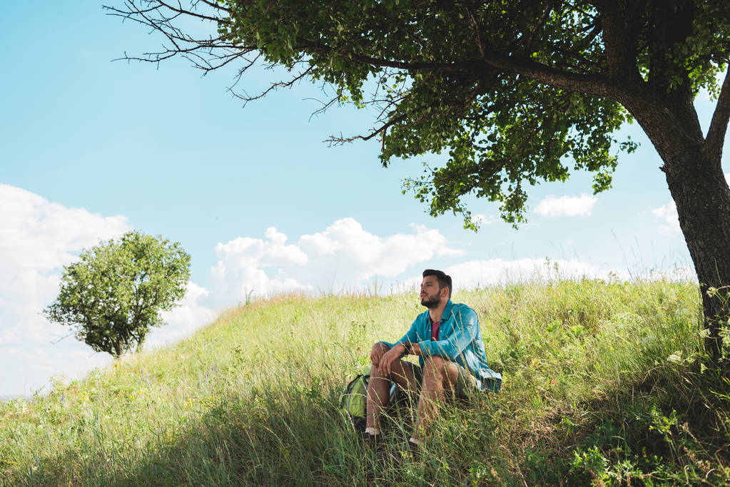 緑夏の草原に座ってバックパックを持つ若い旅行者 - 写真・画像
