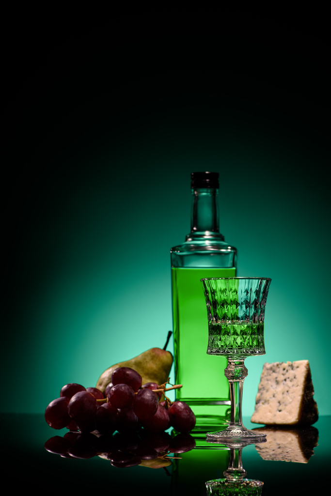 primer plano de absenta con pera, uvas y queso en la superficie del espejo sobre fondo azul oscuro
 - Foto, imagen
