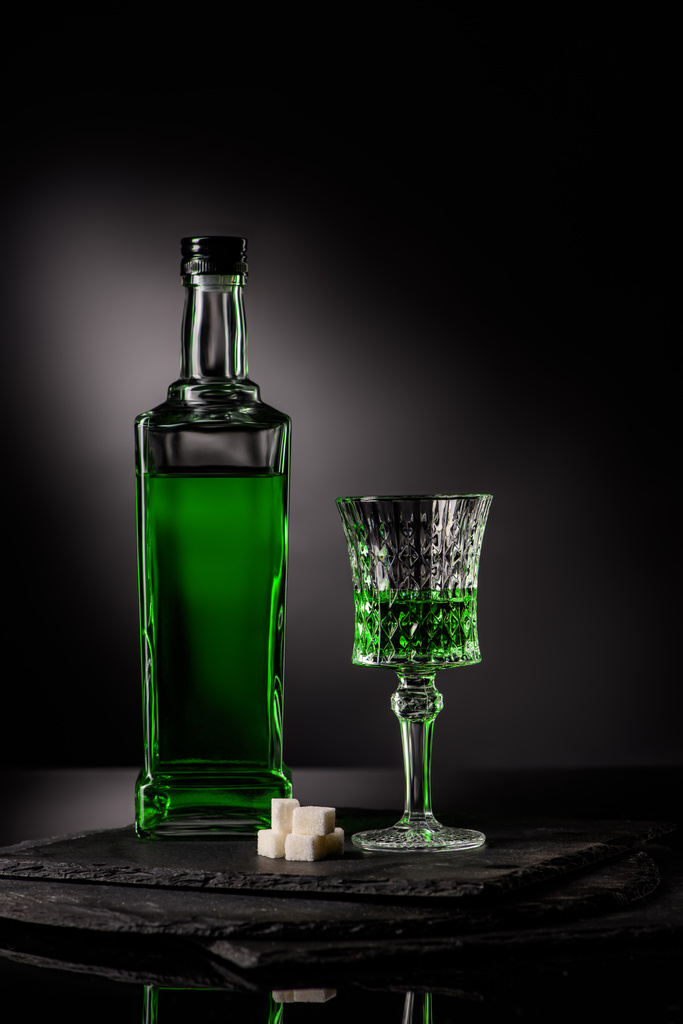 close-up shot of glass and bottle of absinthe with sugar cubes on dark background - Photo, Image