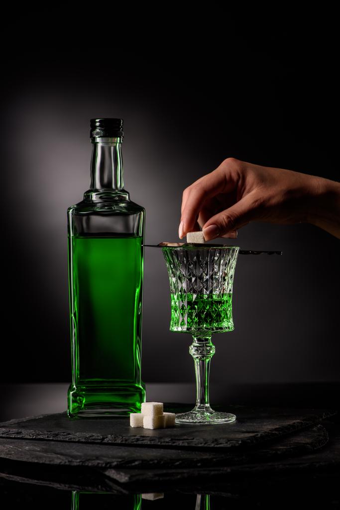 oříznutý snímek žena uvedení kostku cukru na absinthe lžíce na sklo na tmavém pozadí - Fotografie, Obrázek