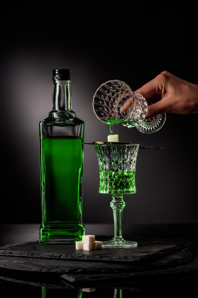 plan recadré de la femme versant l'absinthe dans le verre et sur le cube de sucre sur fond sombre
 - Photo, image