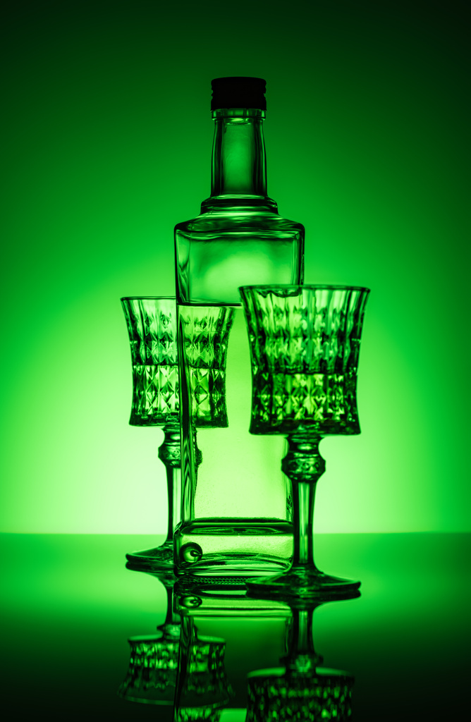 bottle of absinthe with lead glasses on mirror surface and dark green background - Photo, Image