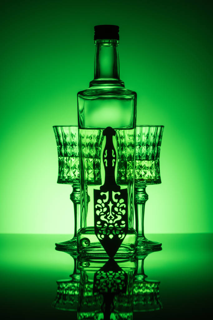 bottle of absinthe with crystal glasses on reflective surface and dark green background - Photo, Image