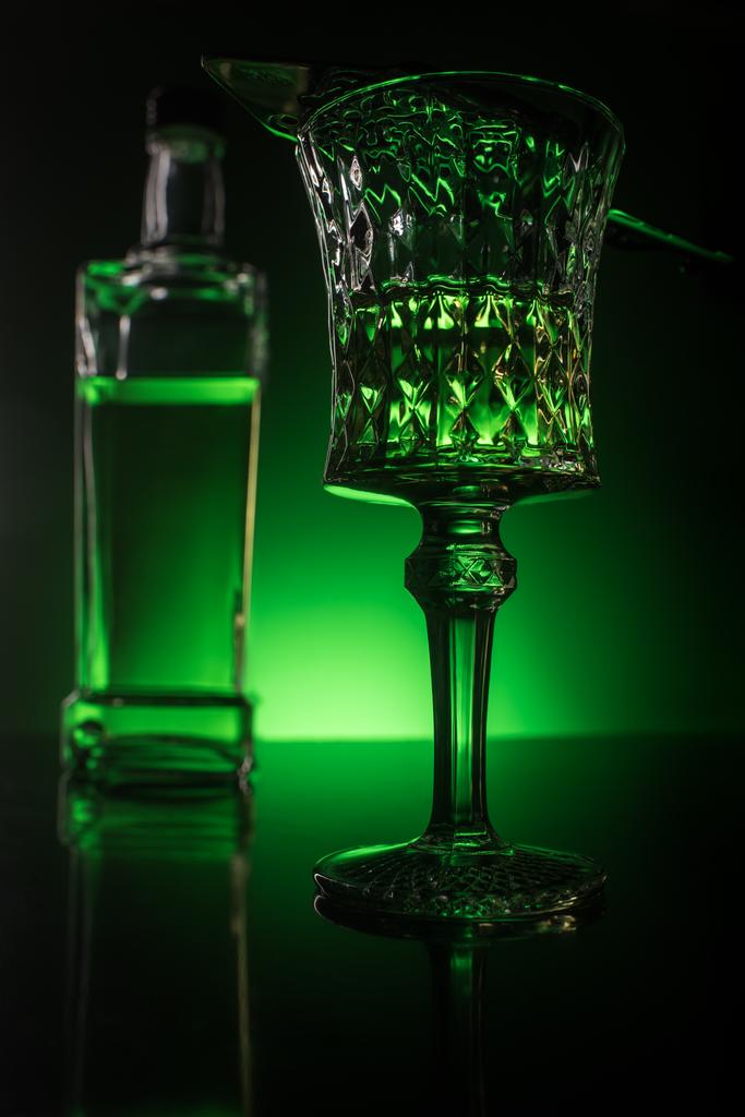 Nahaufnahme von Glas mit Absinth und Flasche auf reflektierender Oberfläche und dunkelgrünem Hintergrund - Foto, Bild