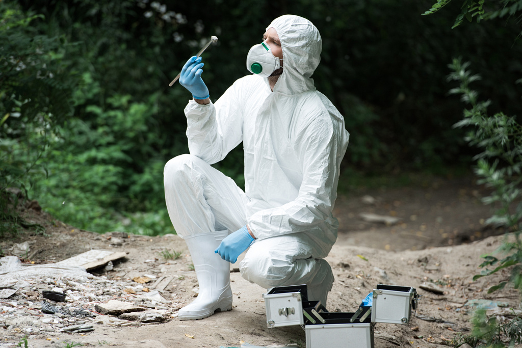focused male scientist in protective suit and mask examining stone while holding by tweezers in forest  - Photo, Image