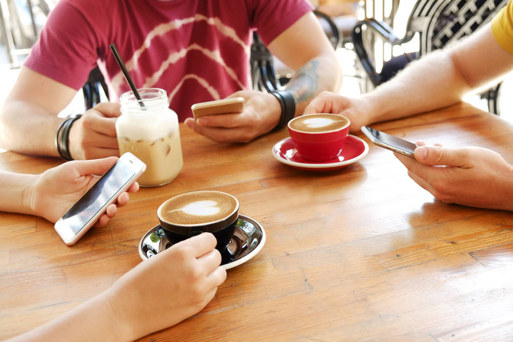 Grupo de amigos bebendo cappuccino no café, olhando para smartphones, verificando gostos & mensagens. Vício em redes sociais. Jovens homens e mulheres segurando telefones celulares e bebidas. Fundo, vista superior
. - Foto, Imagem