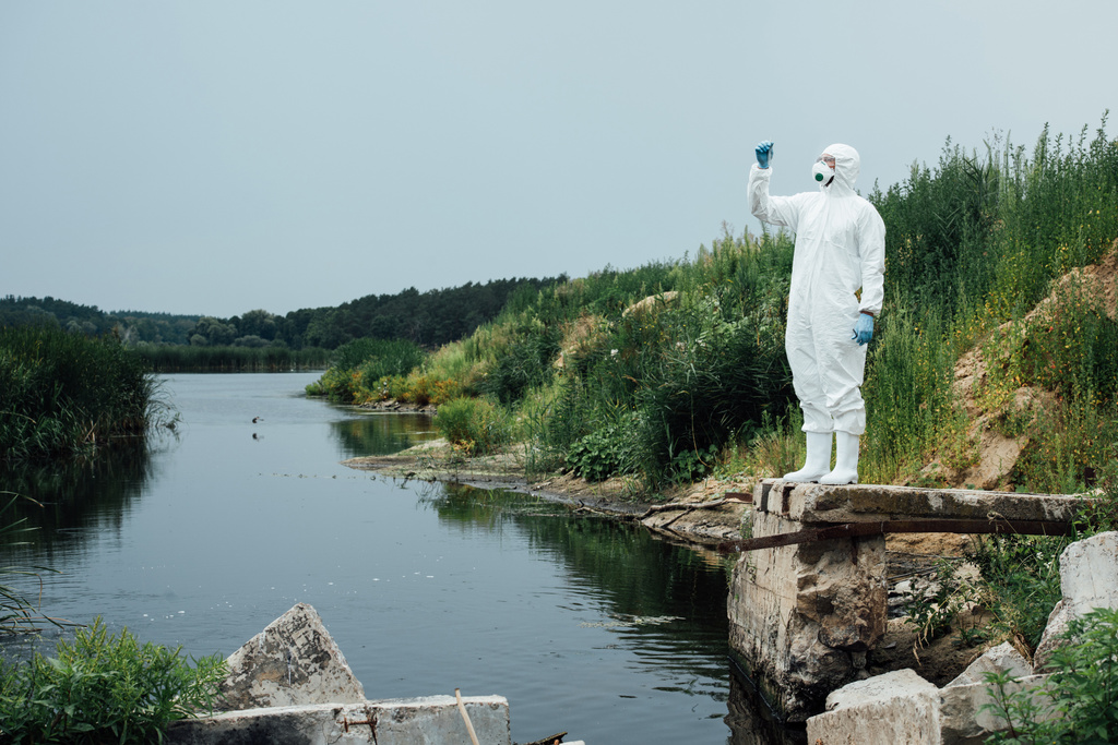 mâle scientifique en masque de protection et costume regardant l'échantillon d'eau dans la fiole d'essai à l'extérieur
  - Photo, image