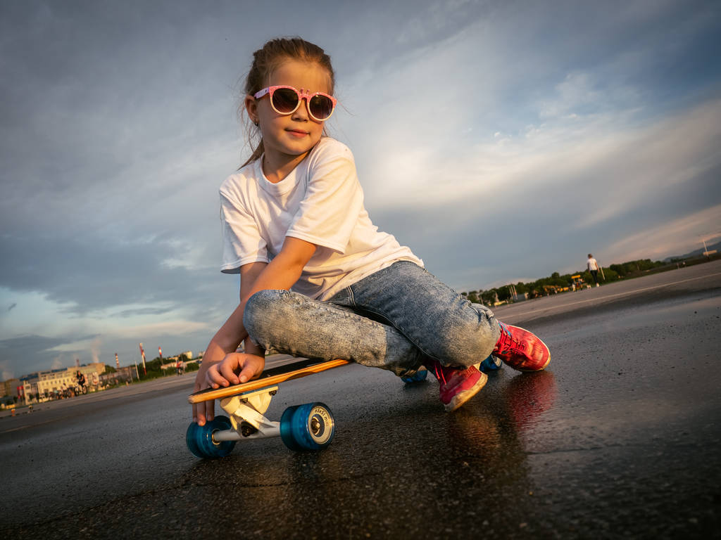 Ulica sportowa: Jolly dziewczyna w okulary usiadł na relaks na longboard po spacerze w parku na łyżwach. - Zdjęcie, obraz