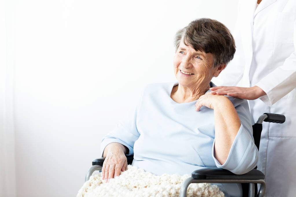 Feliz abuela en silla de ruedas y cuidadora apoyándola. Copiar espacio en la pared
 - Foto, Imagen