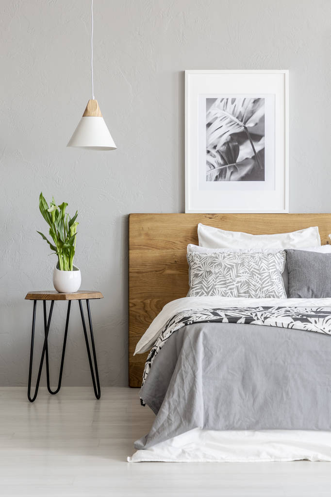 Planta sobre mesa junto a cama de madera en el interior del dormitorio gris con lámpara y póster. Foto real
 - Foto, imagen