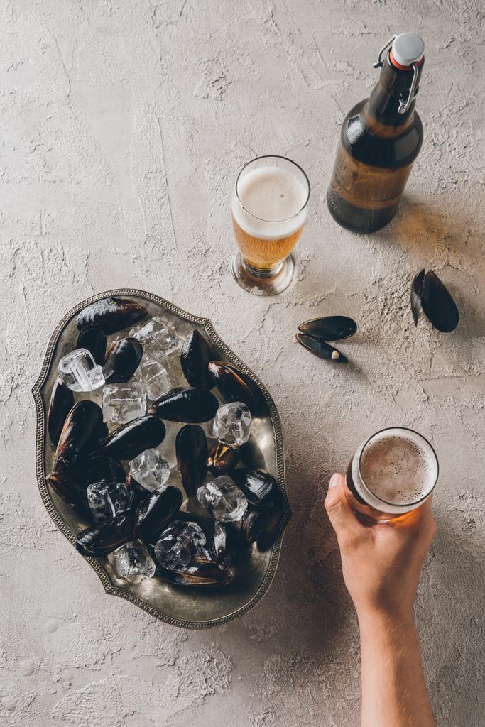 卓上にビールのグラスを持つ男、ボウルに氷とムール貝の部分的なビュー - 写真・画像