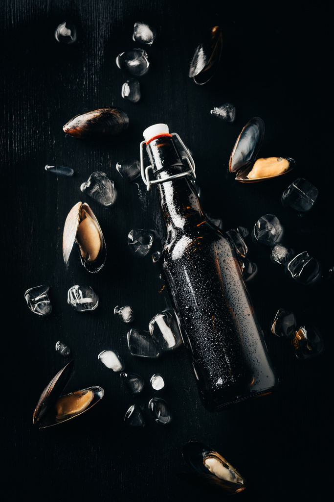 flat lay with bottle of beer, mussels and ice cubes arranged on dark tabletop - Photo, Image