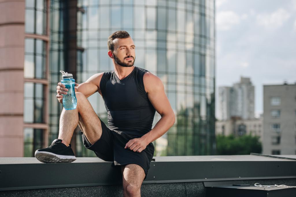 handsome sportsman resting and holding sport bottle of water on roof - Photo, Image