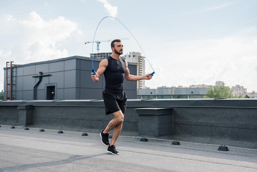 handsome sportsman training with jumping rope on roof - Photo, Image