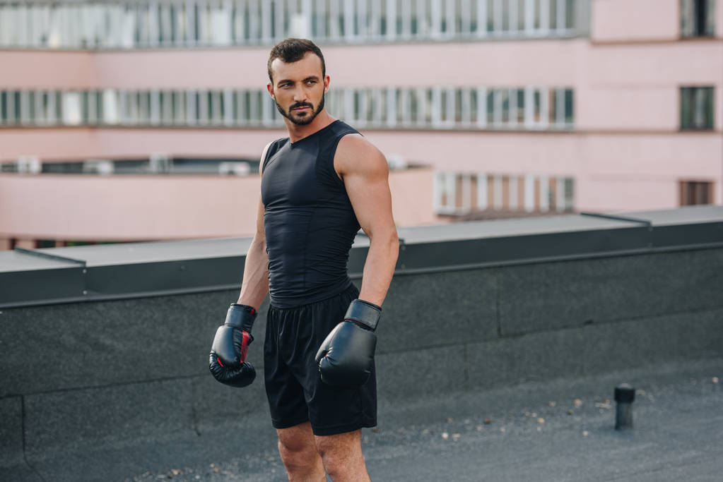 όμορφος αθλητικός τύπος στέκεται με μαύρα γάντια πυγμαχίας στη στέγη - Φωτογραφία, εικόνα