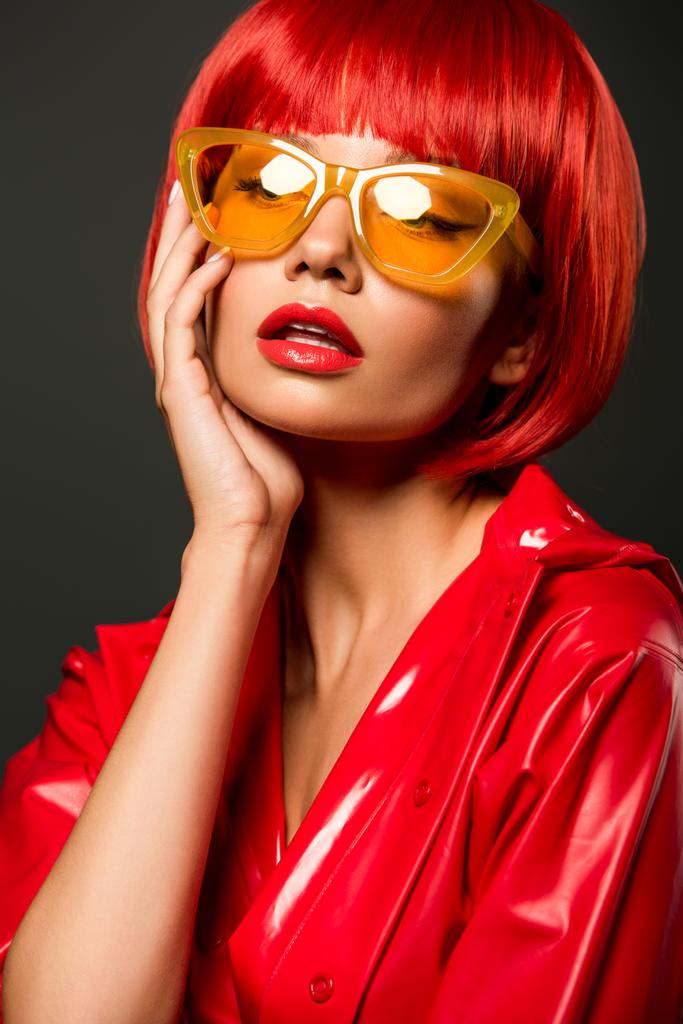 close-up portrait of young woman in red latex jacket and vintage yellow eyeglasses isolated on grey - Photo, Image
