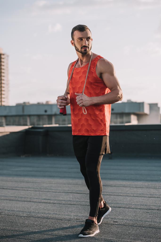 handsome sportive man with jumping rope and red shirt looking away on roof - Photo, Image