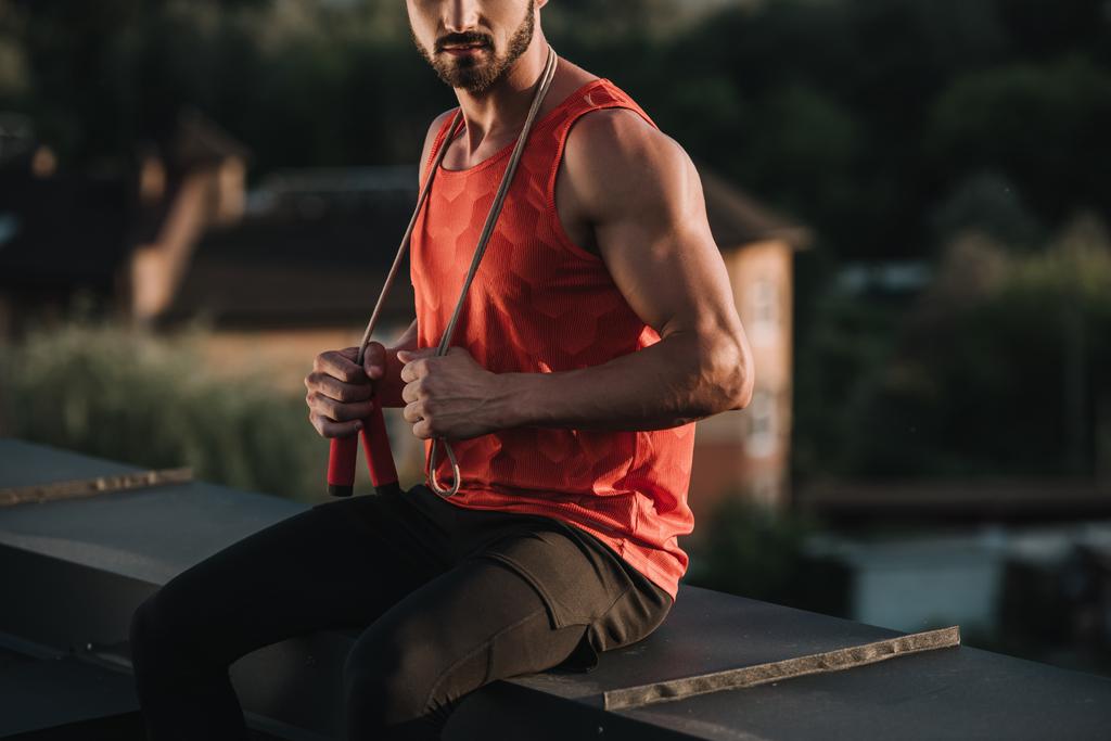 cropped image of sportsman with jumping rope on neck sitting on roof - Photo, Image