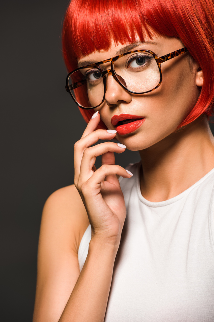 hermosa mujer joven con corte bob rojo y gafas con estilo mirando a la cámara aislada en gris
 - Foto, Imagen