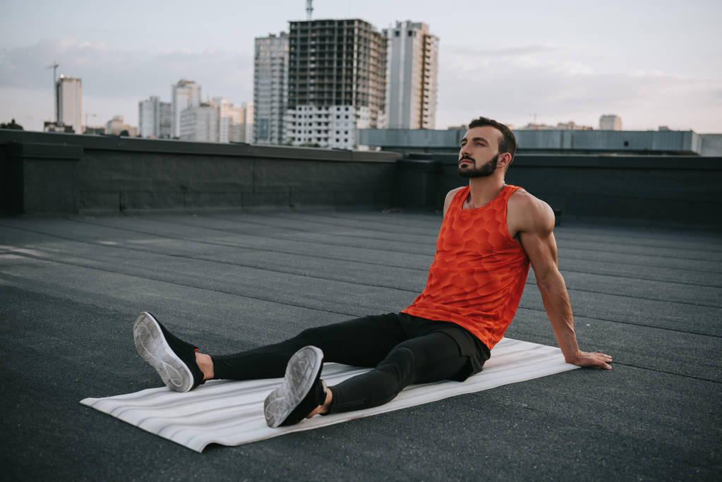 красивий спортсмен відпочиває на йога мат після тренувань на даху
 - Фото, зображення