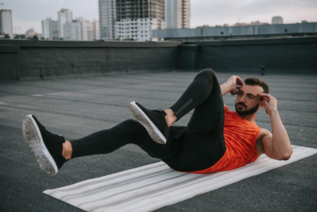 handsome sportsman doing sit ups on yoga mat on roof - Photo, Image