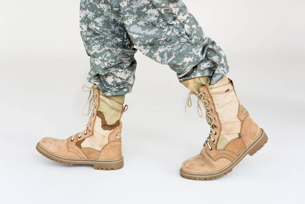 částečný pohled mužského vojáka v maskovací oblečení a boty na šedém pozadí - Fotografie, Obrázek