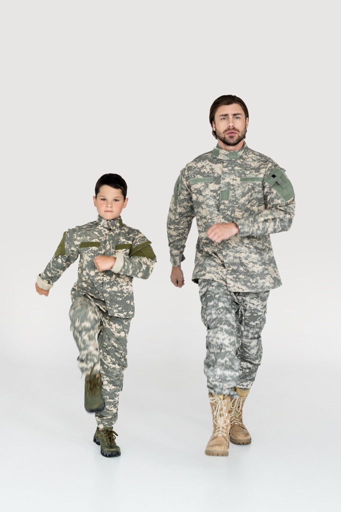 Ojciec i syn w wojskowych mundurach maszeruje i patrząc na kamery na szarym tle - Zdjęcie, obraz