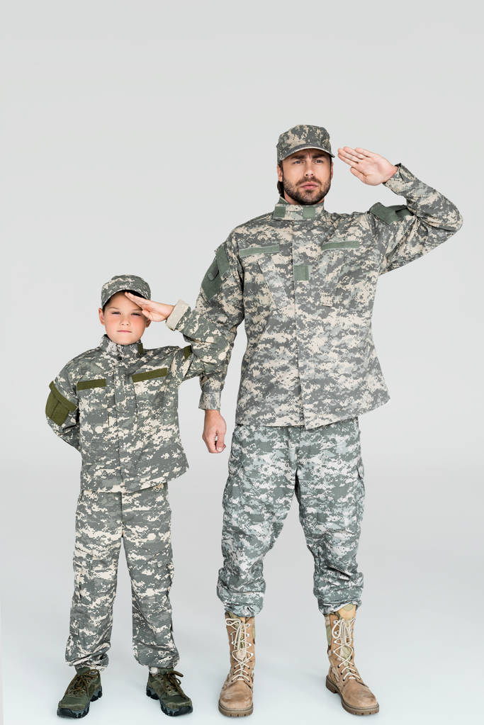 Ojciec i syn w wojskowych mundurach pozdrawiając i patrząc na kamery na szarym tle - Zdjęcie, obraz