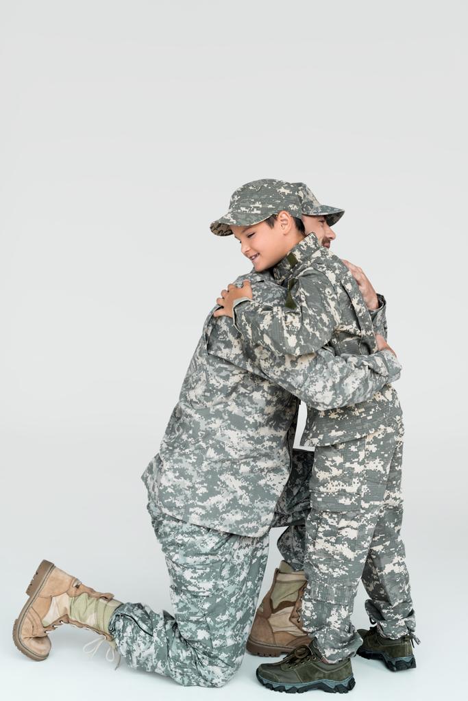 Baba ve oğul her diğer gri arka plan üzerine sarılma askeri üniformalı yan görünüm - Fotoğraf, Görsel