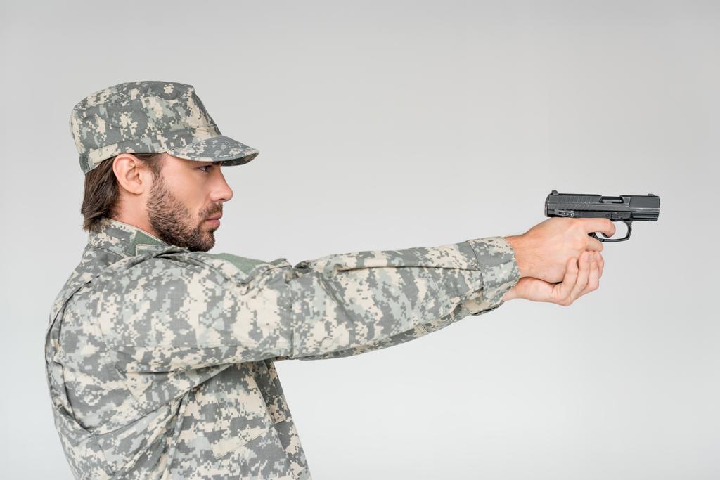 グレーに分離された銃を保持している軍服の男性兵士の側面図 - 写真・画像