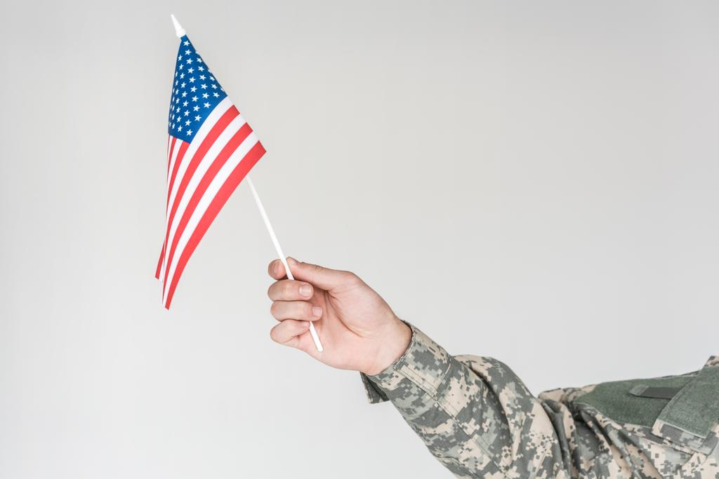 vista parcial de niño en ropa de camuflaje sosteniendo asta de bandera americana en mano aislado en gris
 - Foto, imagen