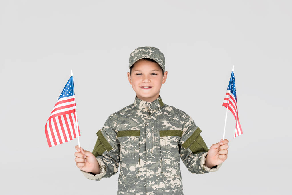portret dziecka uśmiechający się w mundur z american maszty w ręce na szarym tle - Zdjęcie, obraz