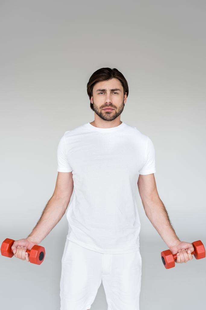 portrait of man in white shirt with red dumbbells in hands exercising on grey backdrop - Photo, Image