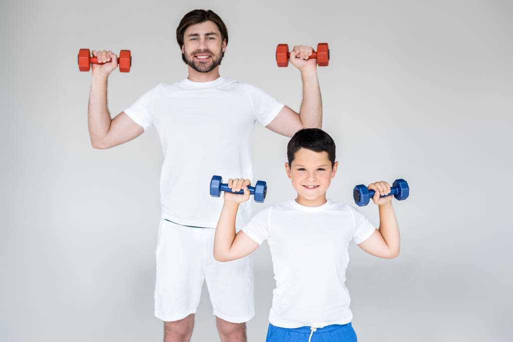 πορτρέτο του χαμογελώντας πατέρας και γιος σε λευκά πουκάμισα άσκηση με βαράκια σε γκρίζο φόντο - Φωτογραφία, εικόνα