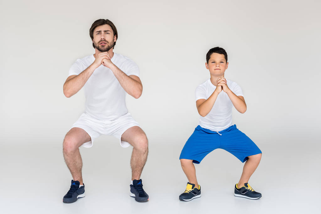 boy and father squatting together on grey background - Photo, Image