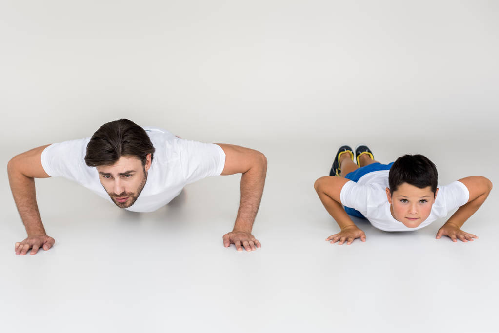 pai e filho fazendo flexões juntos em fundo cinza
 - Foto, Imagem