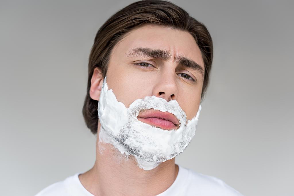 портрет красивого мужчины с пеной для бритья на лице, смотрящего на камеру, изолированную на сером
 - Фото, изображение