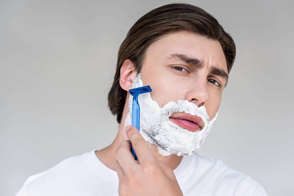 Portret van aantrekkelijke man met schuim op gezicht en scheermes scheren baard op grijze achtergrond - Foto, afbeelding