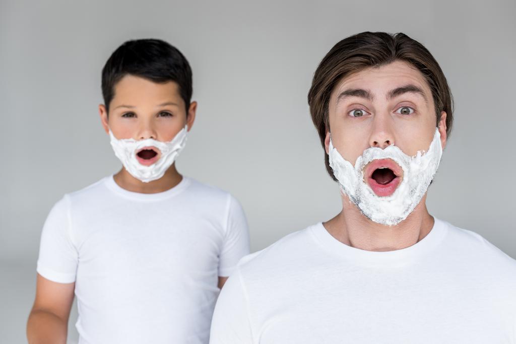 портрет шокированных отца и сына с пеной для бритья на лицах, изолированных на сером
 - Фото, изображение