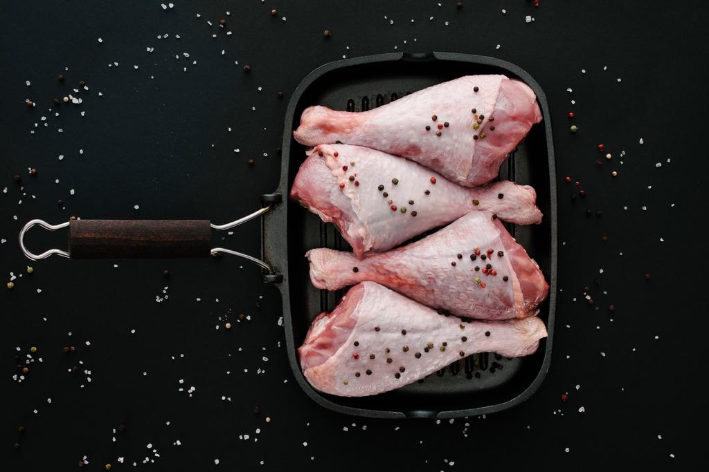 vue du dessus des cuisses de poulet avec des grains de poivre et du sel dans une poêle sur fond noir
 - Photo, image