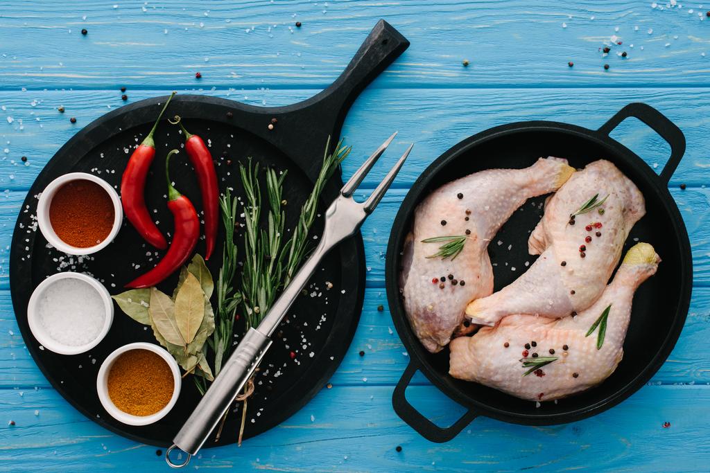 tavuk budu pan ve farklı baharatlar üstten görünüm üzerinde kesme tahtası üzerinde mavi masa üstü et çatalı ile - Fotoğraf, Görsel