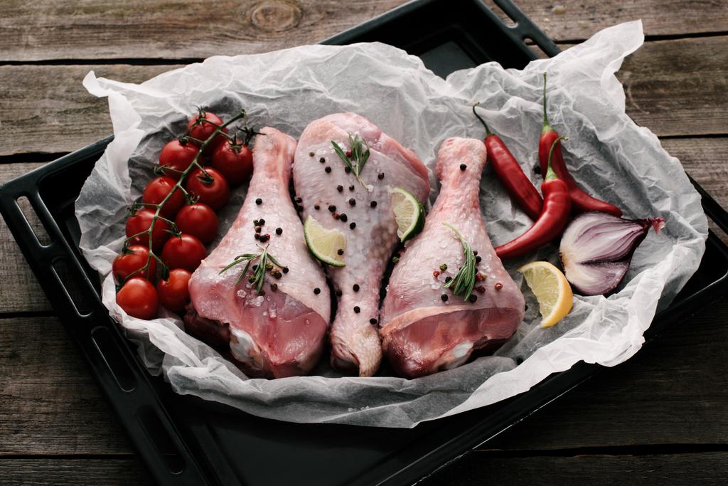 cosce di pollo crude con spezie e verdure fresche su carta su teglia
 - Foto, immagini