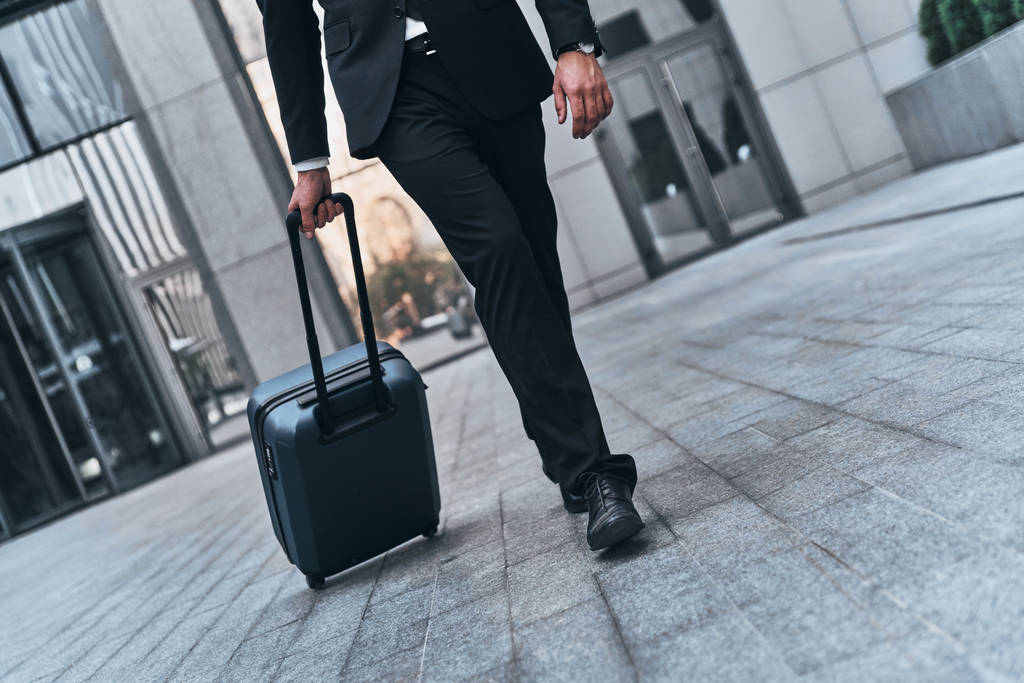 gedeeltelijke weergave van man in pak trekken bagage tijdens het wandelen buiten op kantoorgebouw - Foto, afbeelding