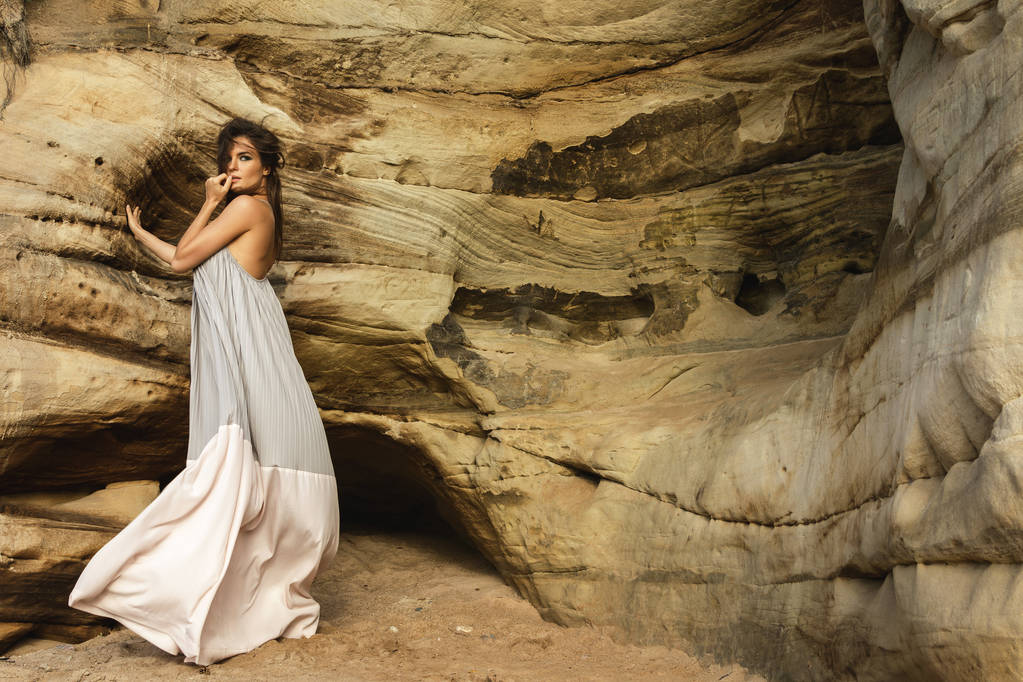 Молодая чувственная женщина в красивом длинном платье рядом с песчаными скалами
 - Фото, изображение