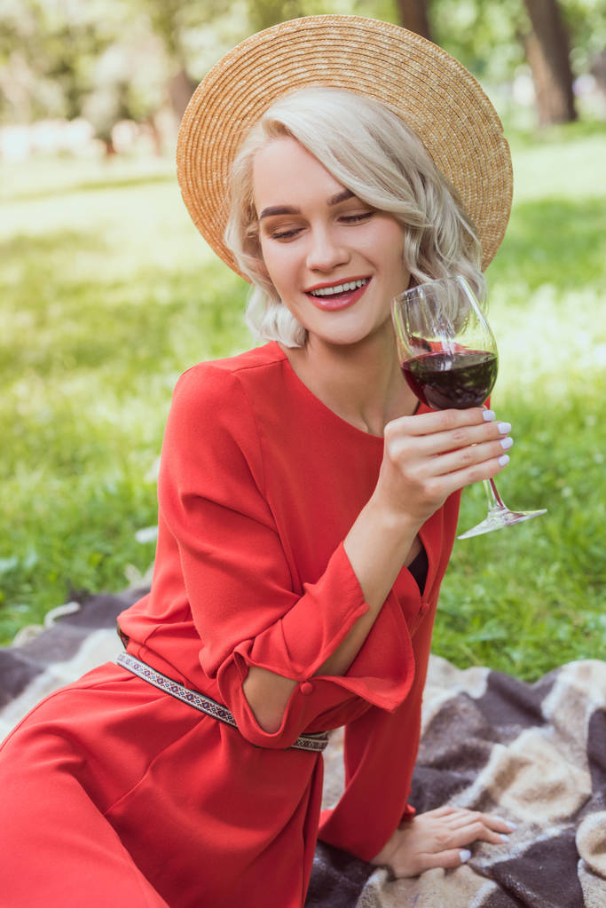 menina atraente em vestido vermelho segurando copo de vinho tinto no parque
 - Foto, Imagem