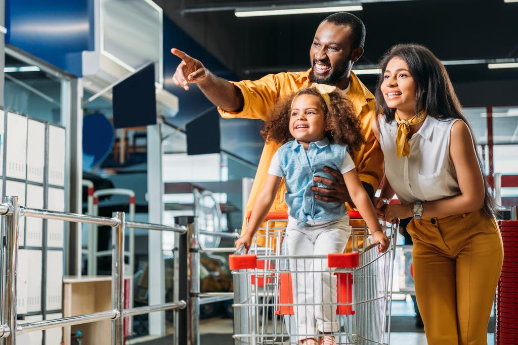 glimlachen van Afro-Amerikaanse man kleine dochter en vrouw in de supermarkt door de vinger te wijzen  - Foto, afbeelding